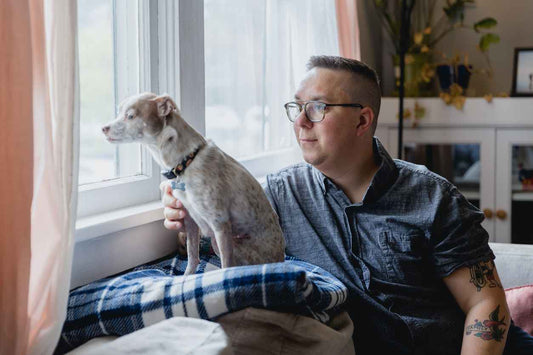 Portrait of an autistic man with his dog indoors. They are sitting on their couch in the living room of his home.