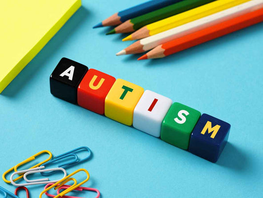 The word autism on colorful cubes with stationery objects on blue background.