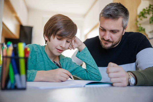 Neurodivergent child sitting at home and doing homework with his father taking care of him, spending time together